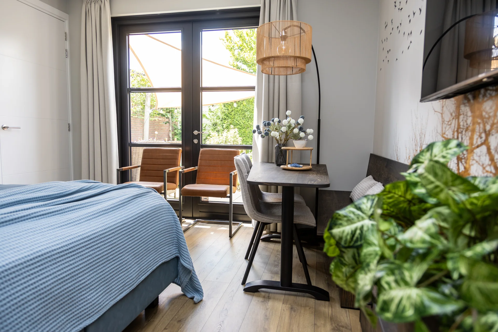Kamer van ’t Klijnhuysje met blauw bed, openslaande deuren naar de tuin en een warme hanglamp